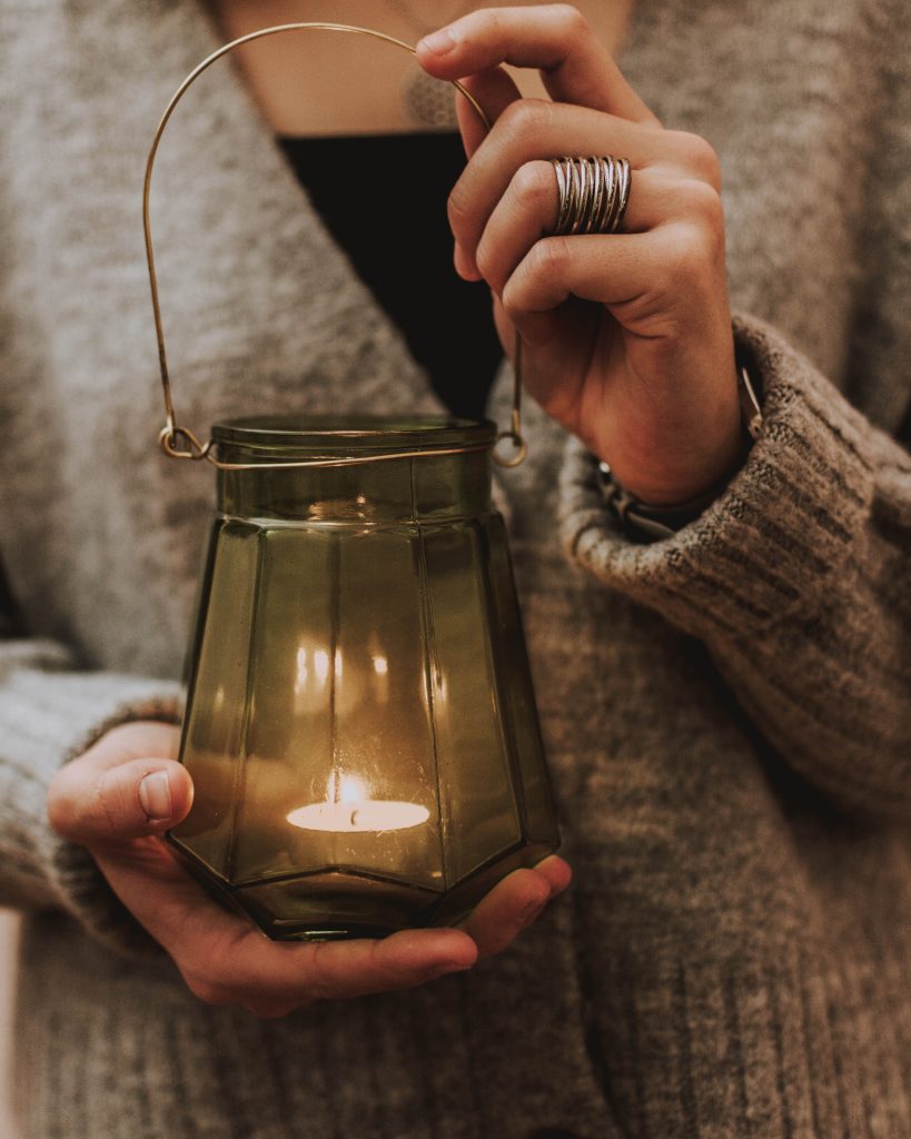 Manos sosteniendo un farol de cristal con una vela encendida representando la luz y la transformación personal